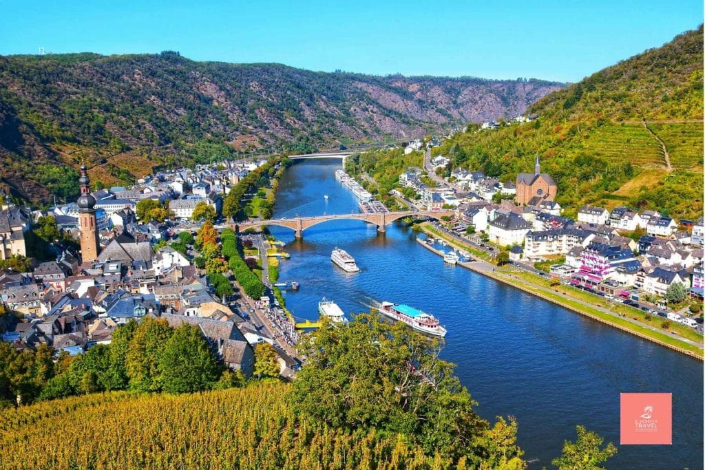 River ships sail down the Moselle river, transversing a scenic mountain valley.