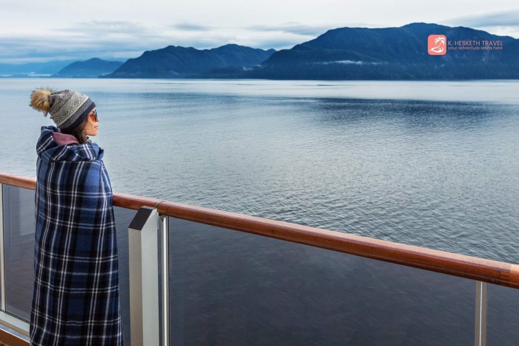 Woman stands at the rail, watching the scenery as she sails the Inside Passage on an Alaska cruise.
