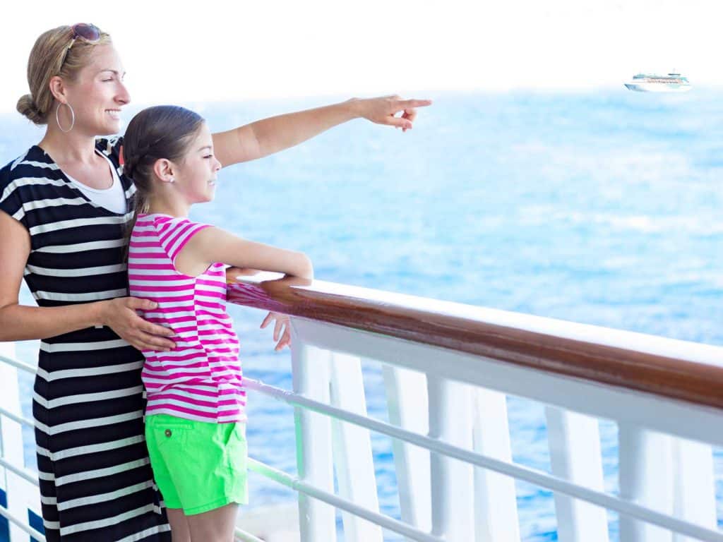 mother points out a site to daughter from shipboard rail on a family cruise line