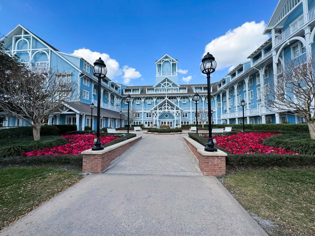Blue building with white trim, flanked by red flowers and a blue summer sky is Disney's Beach Club resort, an excellent choice for a first trip to Disney World