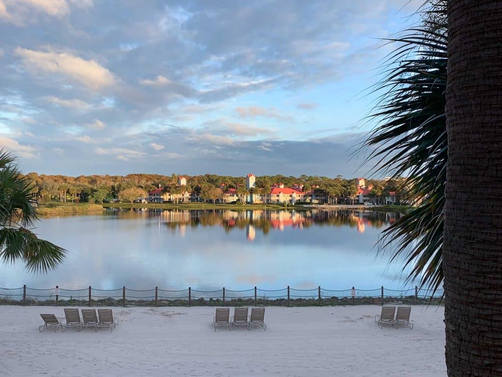 Brightly colored buildings reflect across surface of a lake at Disney's Caribbean Beach Resort, one of the best resorts at Disney World for tropical vibes.